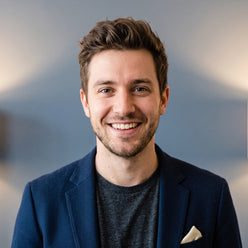 Portrait of Jordan P., a person with a genuine, enthusiastic expression, against a clean slate blue background.
