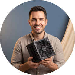 A masculine-presenting influencer from Build Masters smiles, holding a 1000W fully modular ATX power supply against a slate b