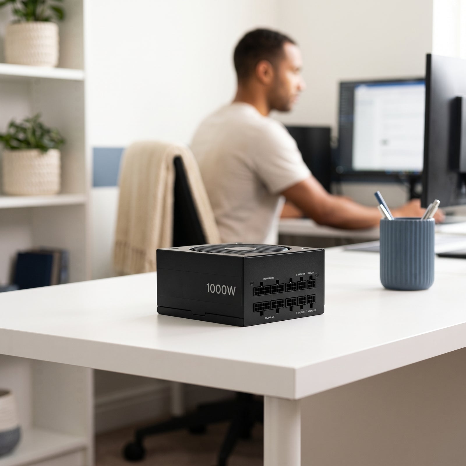 A 1000W fully modular ATX PSU computer power supply on a modern, minimalist desk with subtle blue and cream accents. A person