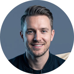 Portrait of male tech influencer Alex Tech smiling. He is shown from the shoulders up against a slate blue background.